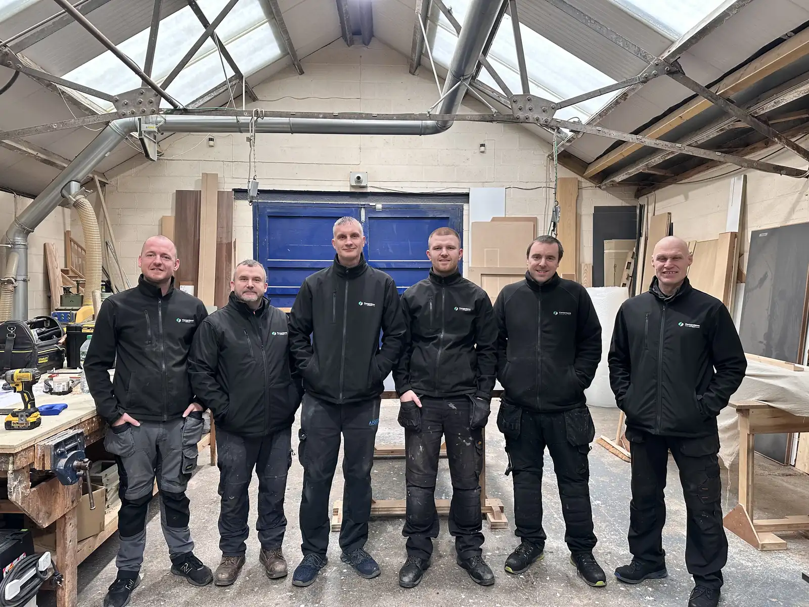 Cornerstone joinery team in branded black jackets standing together in the workshop