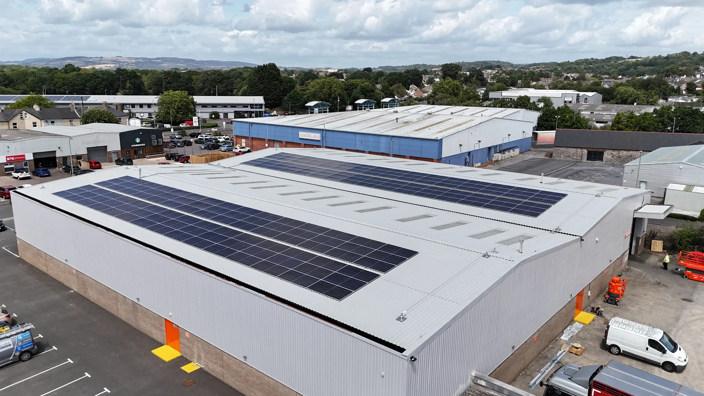 Aerial view of the Booker Newton Abbott warehouse with rooftop solar arrays and the Devon hills beyond