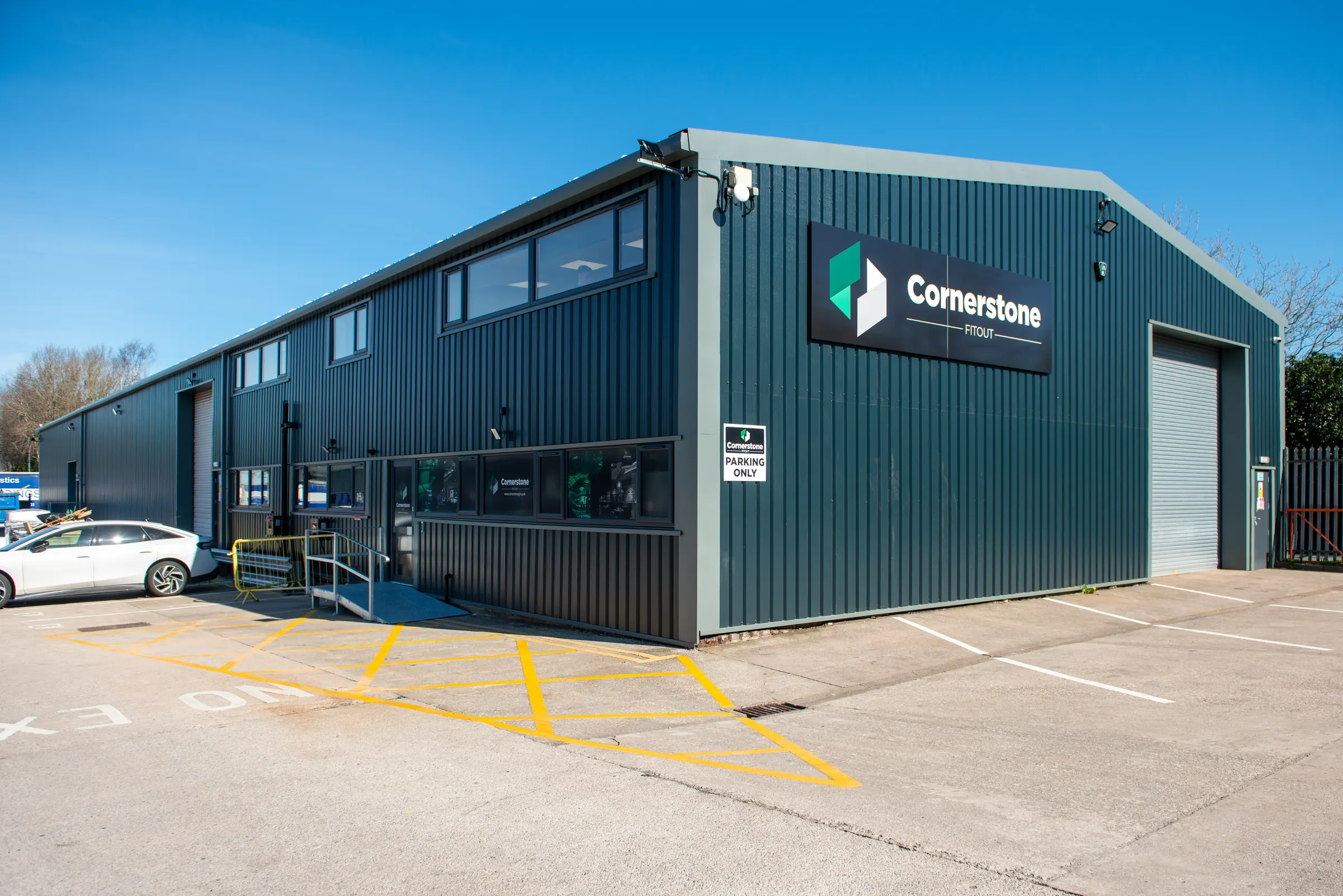 Cornerstone workshop building with dark green cladding and company sign under blue sky