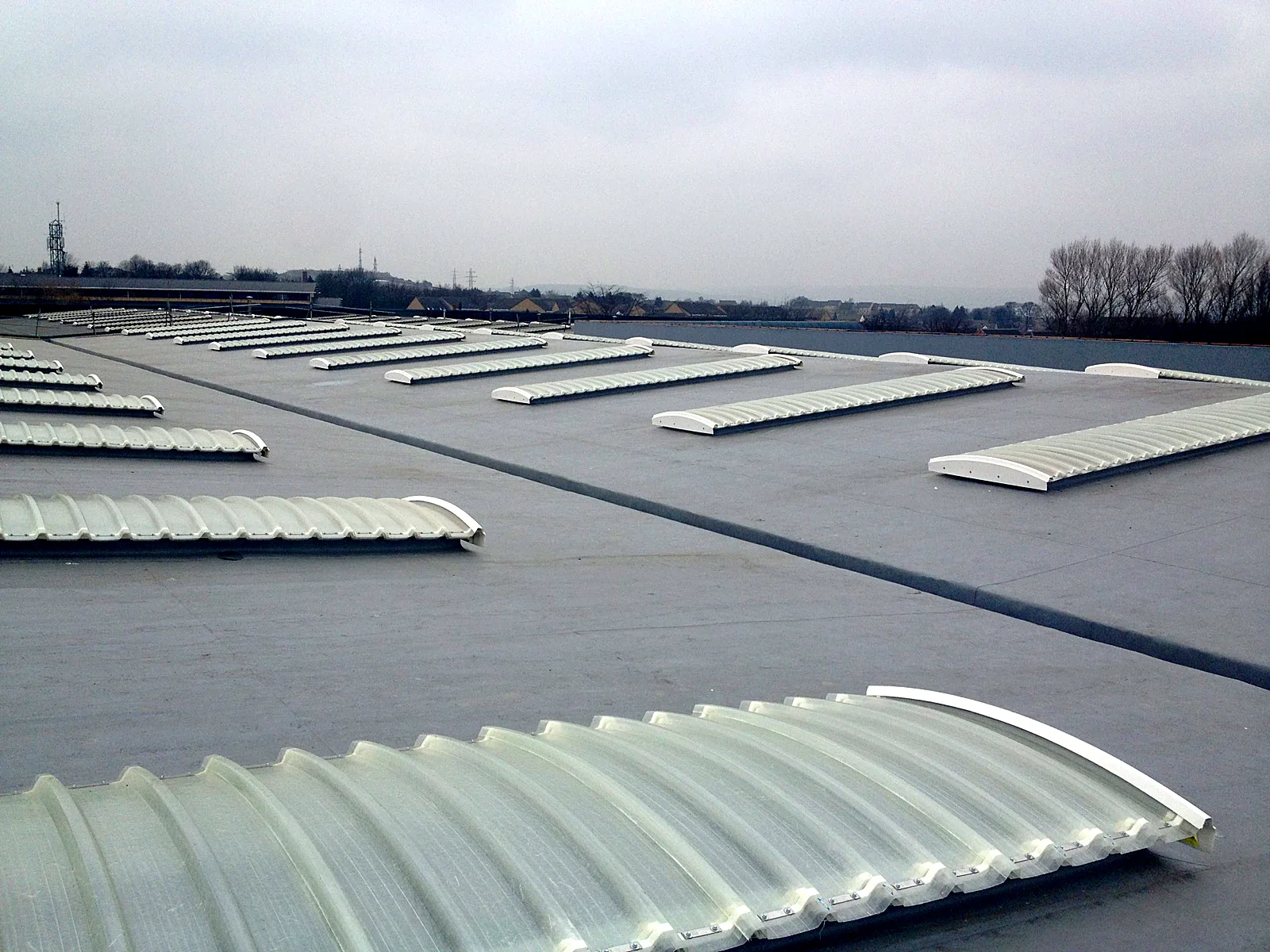 Grey single-ply roof with rows of barrel rooflights on a large retail unit