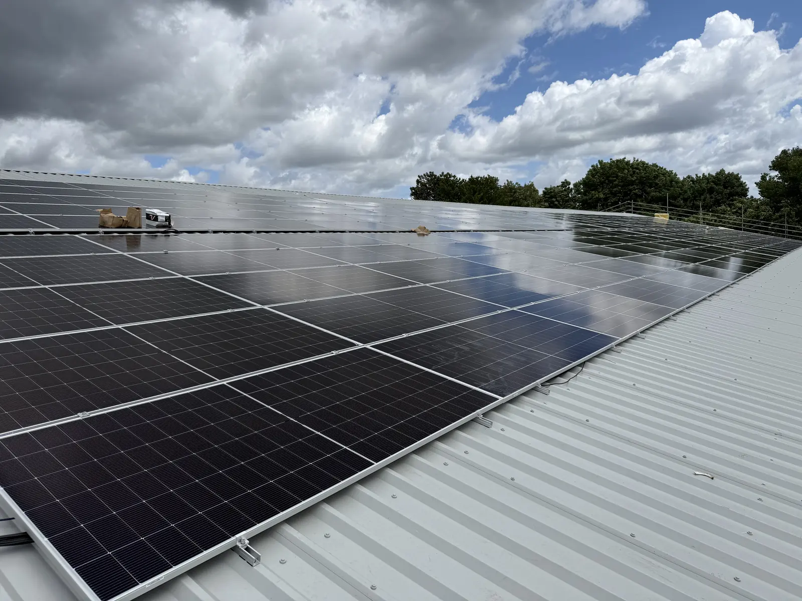 Rows of new solar panels installed on the metal roof under a cloudy sky