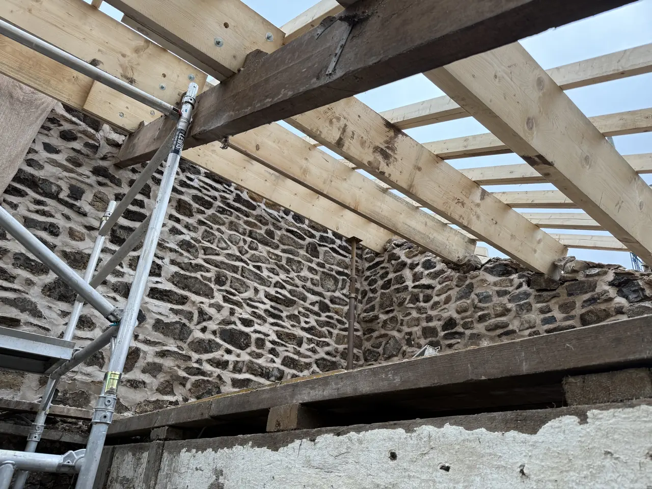 Inside the barn looking up at new rafters, with oak beam and rubble stone walls