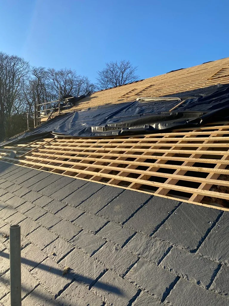 Natural slates being laid over new battens on the barn roof