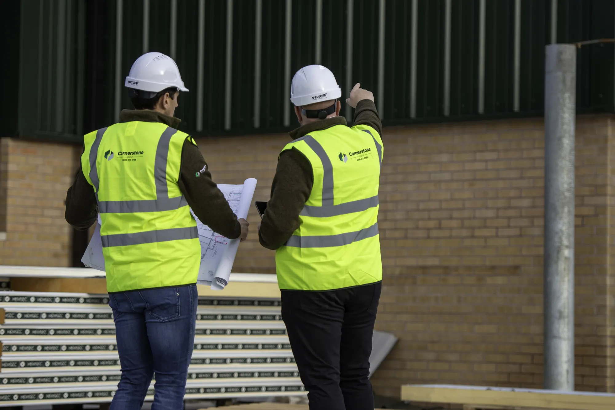 Two Cornerstone managers in hard hats and branded hi-vis reviewing drawings on site