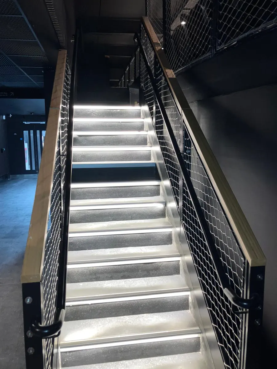 Staircase at Olympia with LED lit treads, mesh balustrades and timber handrails