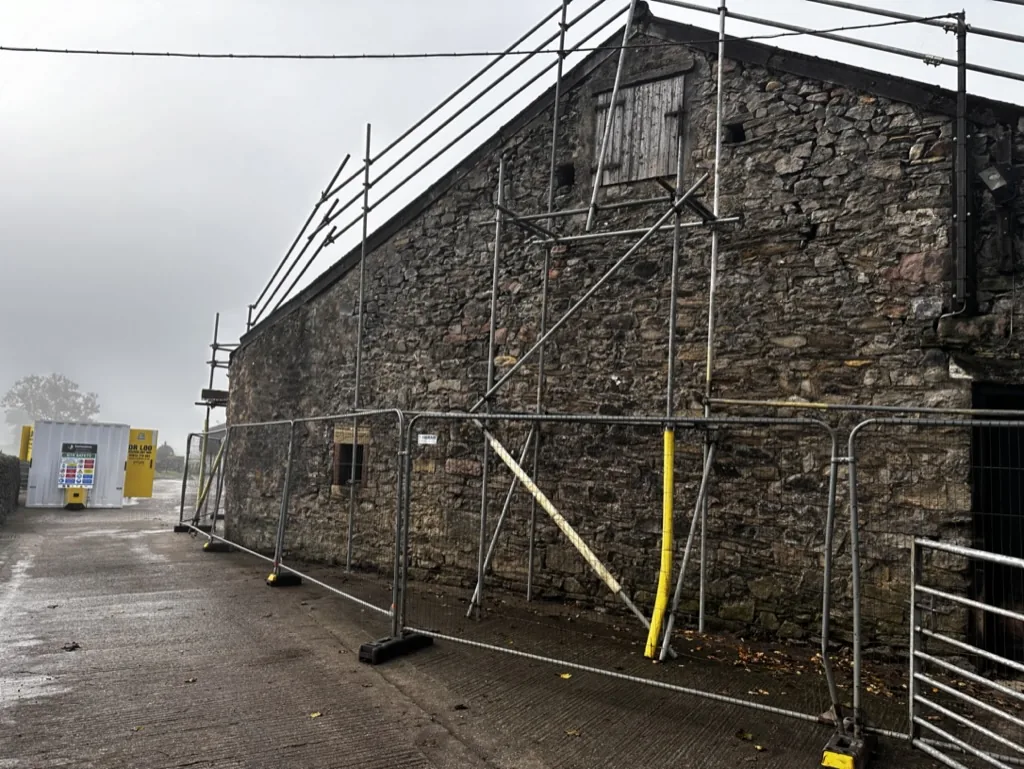 Stone barn at Fober Farm with scaffolding and site fencing set up before roof works