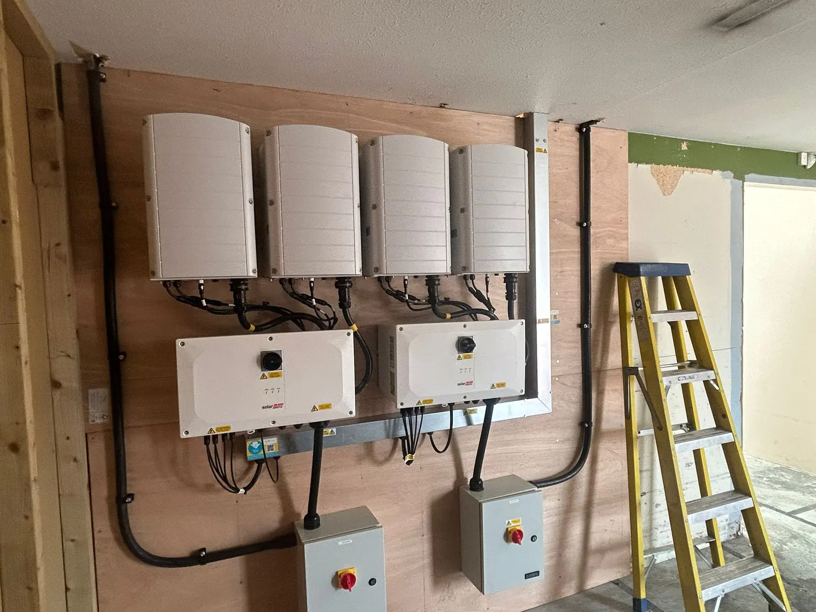 Solar inverters, isolators and cabling neatly installed on a plywood backboard in the plant room