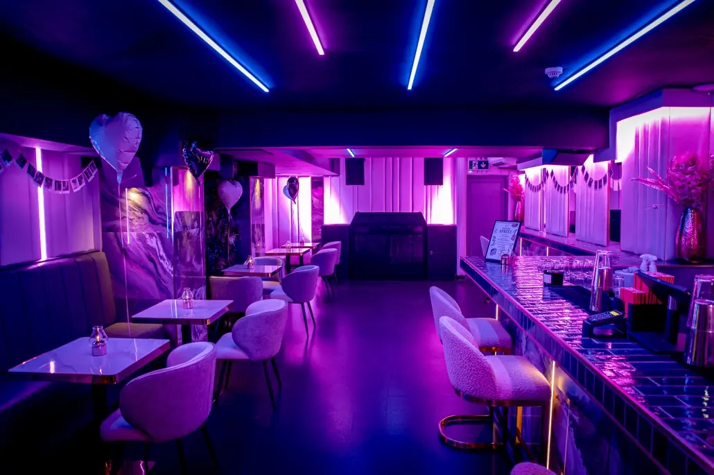 Baluga bar lit in purple and blue neon with white tub chairs and a long bar counter