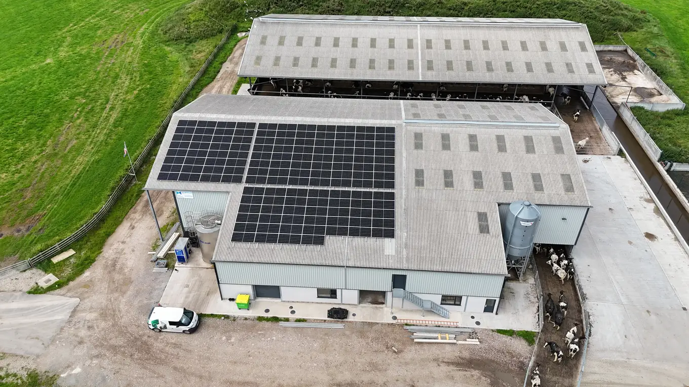 Drone view looking down on solar panels across a farm building roof beside open fields